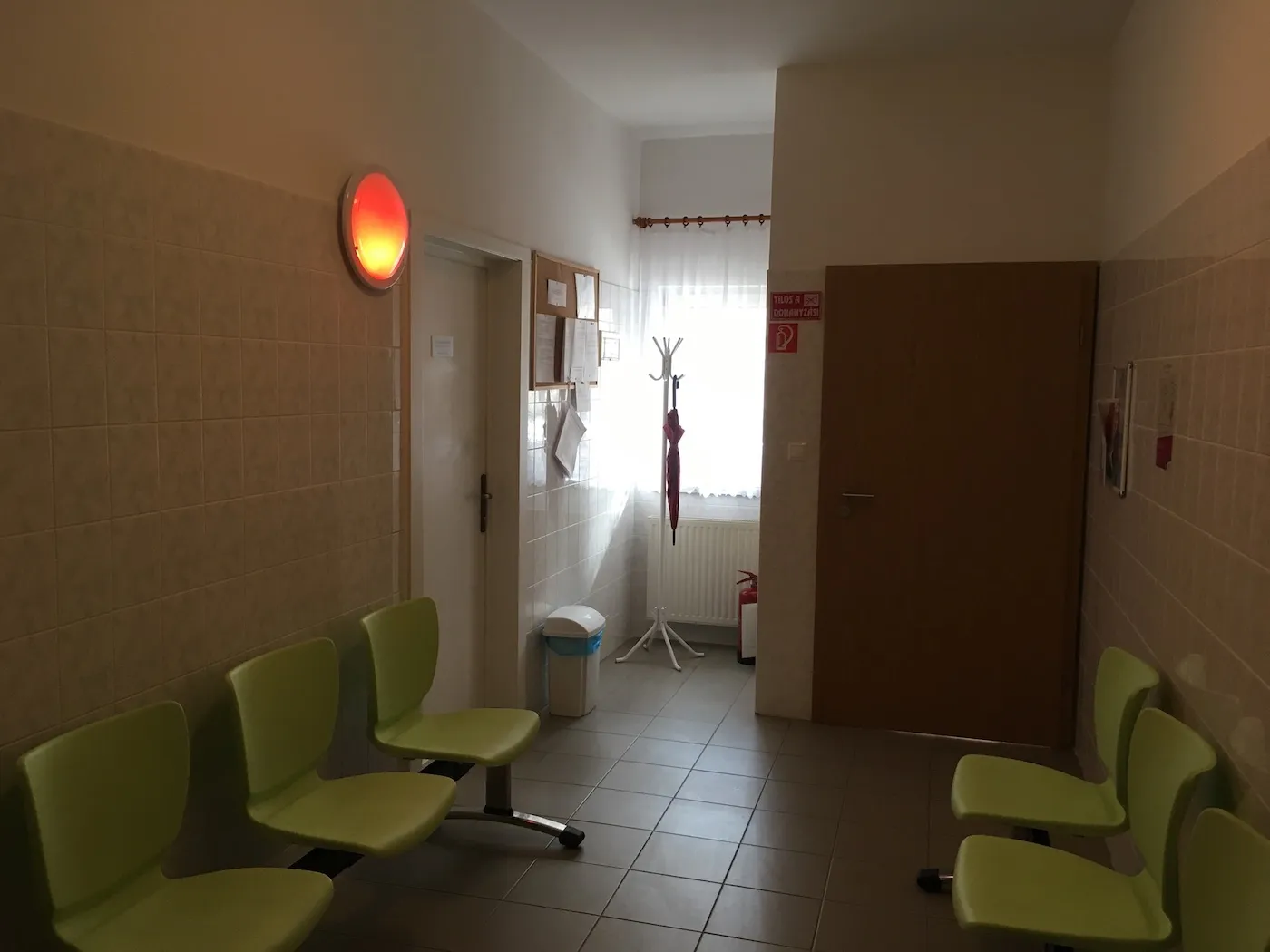 A doctor's office's waiting room with the lamp on the wall showing a busy office (red)