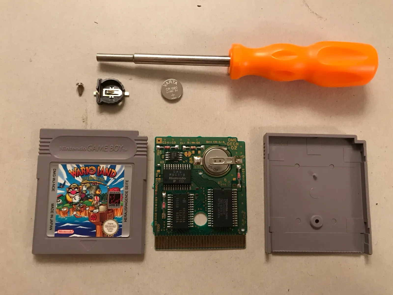 Battery replacement parts: the opened cartridge, a battery holder and a fresh coin cell